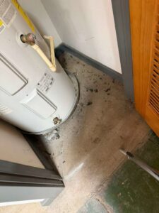 A dirty floor area next to a water heater, showing dust and debris before cleaning by New Image Cleaning Service LLC in Richmond, VA.