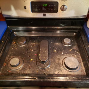 A very dirty and greasy stovetop covered in food debris, showing a 'before cleaning' state by Quickcleanup full service cleaning in Juneau, AK.