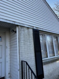 An exterior view of a house with dirty white siding and brick, showing a need for cleaning or replacement by Coastal Construction Group LLC in Cheshire, CT.