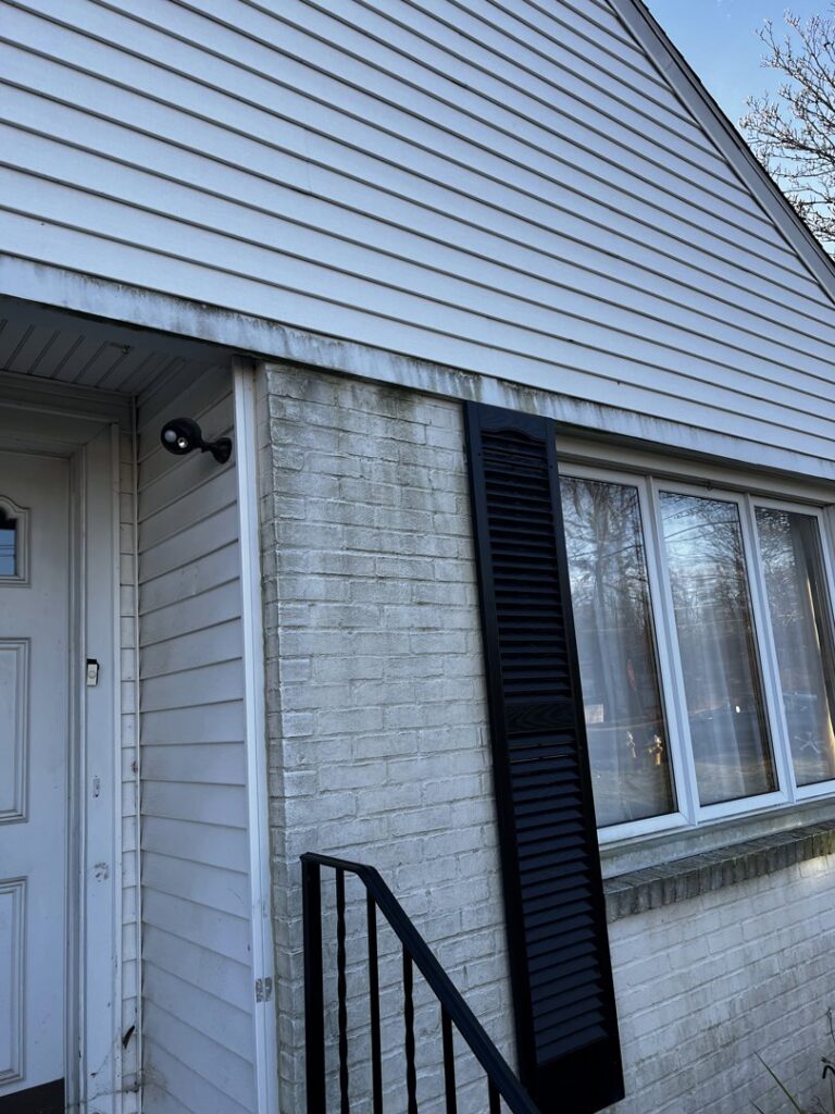 An exterior view of a house with dirty white siding and brick, showing a need for cleaning or replacement by Coastal Construction Group LLC in Cheshire, CT.