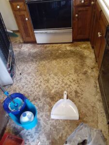A very dirty kitchen floor with a mop bucket and dustpan, indicating a cleaning job by L & G Cleaning Service in Aurora, CO.