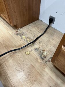 A dirty kitchen floor with crumbs and debris under a cabinet, showing an area requiring deep cleaning by Little Cubs Cleaning Services in Rochester, MN.