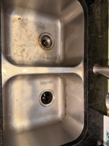 A dirty stainless steel kitchen sink before professional cleaning by Jocelyn's Cleaning Services in Charlotte, NC.