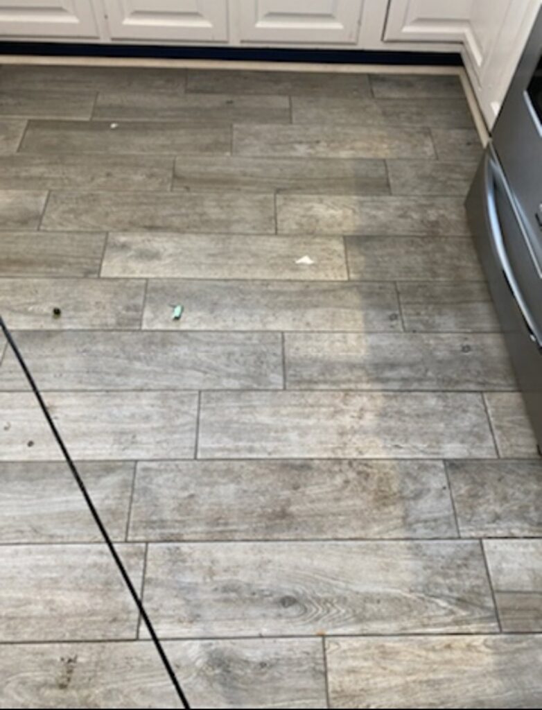 A dirty kitchen tile floor showing grime and debris before professional cleaning by Cuse Cleaning in Syracuse, NY.