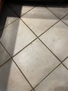 A dirty kitchen tile floor with visible grime and spots, indicating a need for professional cleaning from JLJ Sister's Cleaning & More in Lexington, KY.
