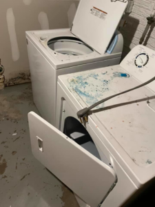 A dirty laundry room with a grimy washer and dryer, showing a 'before' cleaning state for Every Time Cleaning in Cedar Rapids, IA.