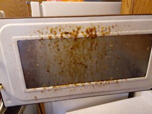 An extremely dirty microwave door covered in food splatters, highlighting a need for cleaning by L & G Cleaning Service in Aurora, CO.