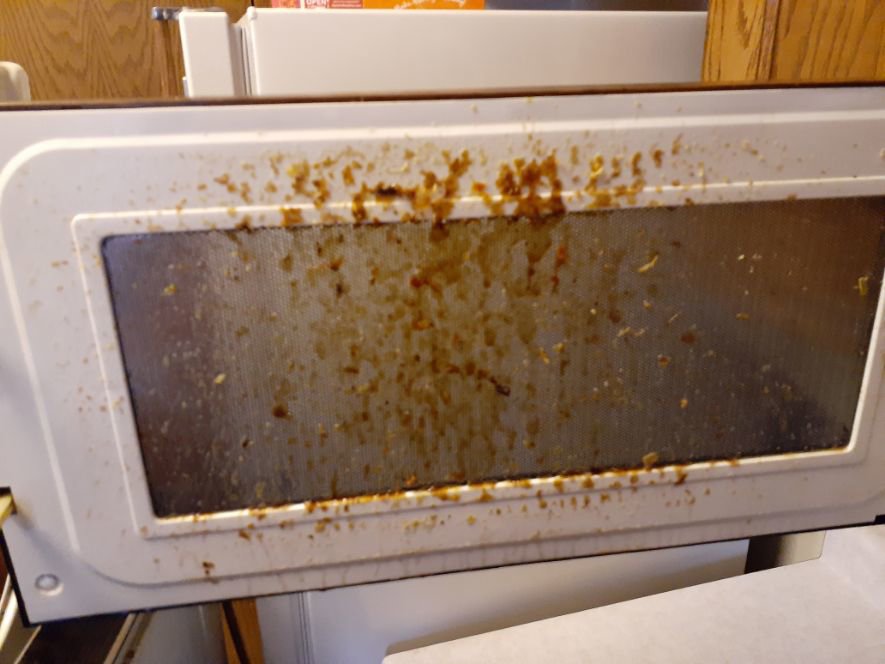 An extremely dirty microwave door covered in food splatters, highlighting a need for cleaning by L & G Cleaning Service in Aurora, CO.