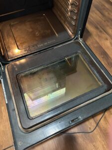 A dirty oven door interior with grease and grime before professional cleaning by Teri Lynn's Cleaning in Williston, ND.