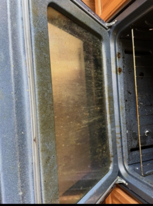 A very dirty oven door interior showing grime and grease, ready for cleaning by Crystal Clear Cleaning Services in New Haven, CT