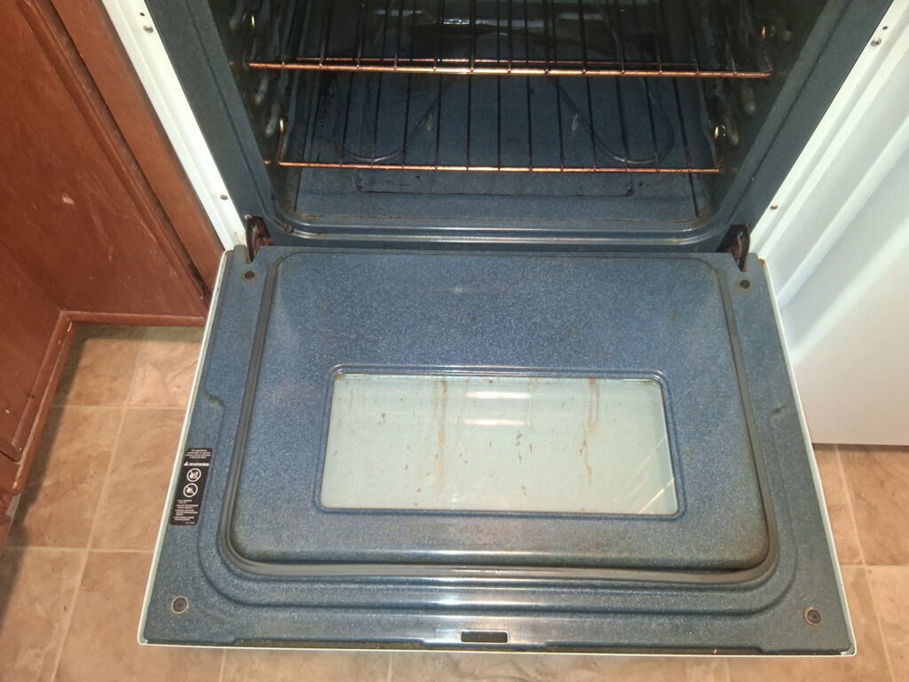 A dirty oven interior with visible grease and grime, showing a before-cleaning state by CleanSlate Cleaning Company in Lansing, MI.