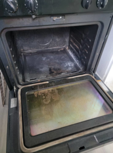 A dirty oven interior with grease and burnt residue before professional cleaning by Windham Cleaning in Akron, OH.