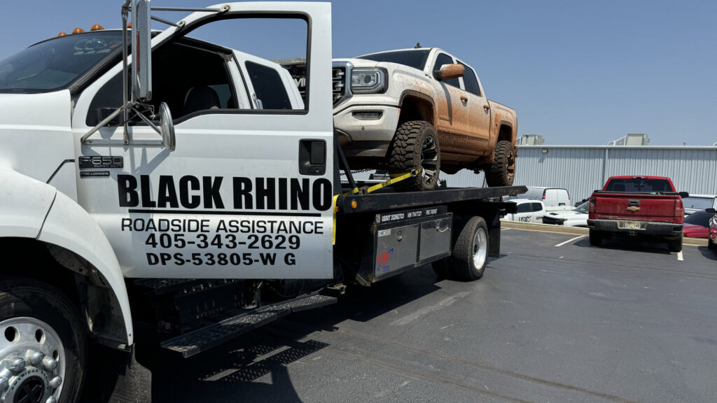 A dirty white pickup truck being towed on a Black Rhino Towing flatbed truck in Denver, CO.