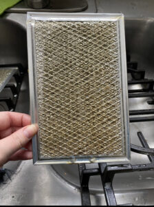 A hand holding a greasy and dirty range hood filter before professional cleaning by Cuse Cleaning in Syracuse, NY.