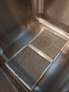 Dirty range hood filters soaking in a sink, demonstrating a deep cleaning task performed by AG Simply Clean in Concord, NC.