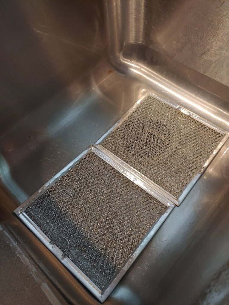 Dirty range hood filters soaking in a sink, demonstrating a deep cleaning task performed by AG Simply Clean in Concord, NC.