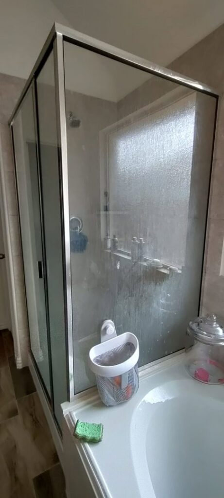 A dirty glass shower door and tub area with visible grime, indicating a 'before' state for Rita's cleaning in Fort Worth, TX.