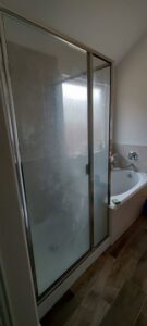 A dirty glass shower door with water spots and grime, indicating a 'before' state for Rita's cleaning in Fort Worth, TX.