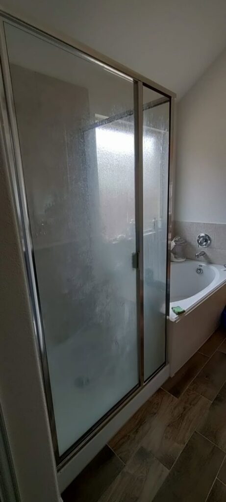 A dirty glass shower door with water spots and grime, indicating a 'before' state for Rita's cleaning in Fort Worth, TX.