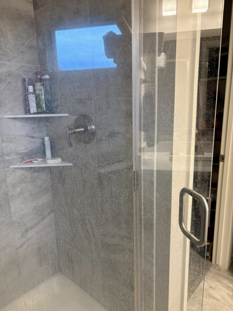 A dirty shower door with water spots and grime before cleaning by Warm & Cozy House Cleaning in Madison, WI
