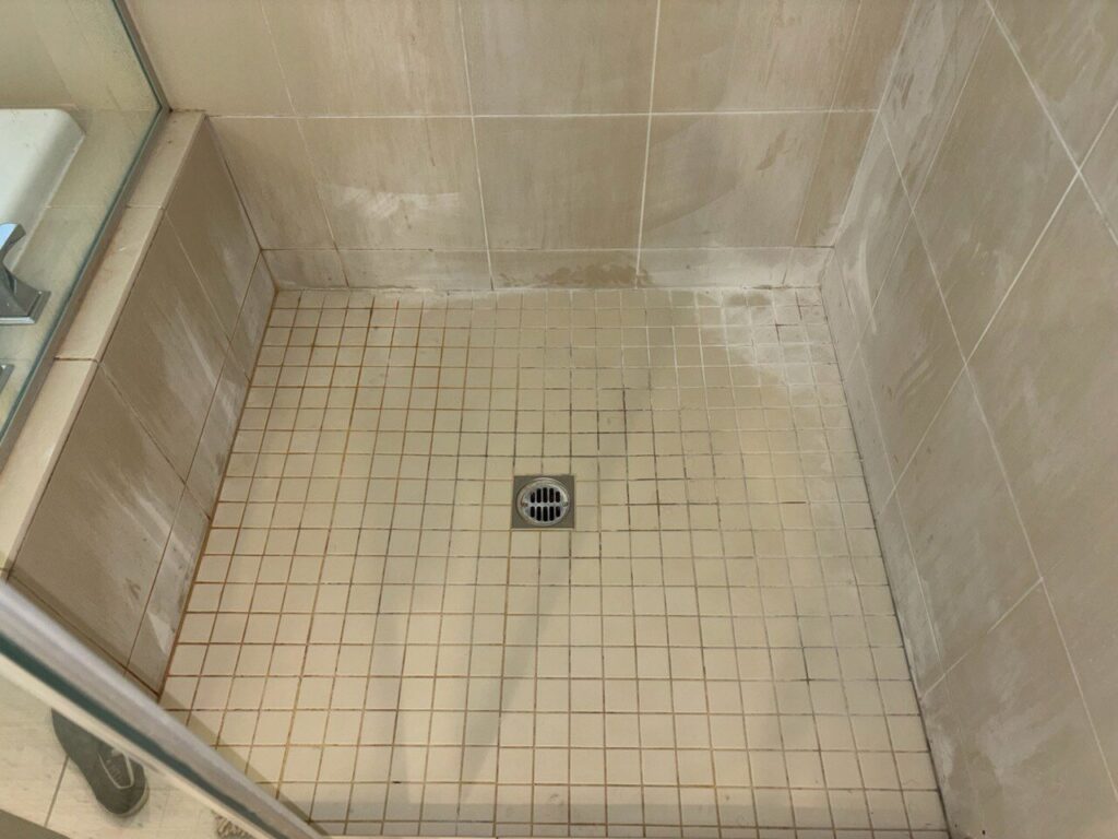 A dirty shower floor with visible grime and soap scum, showing a 'before' state for cleaning by Maid 2 Clean San Diego, CA