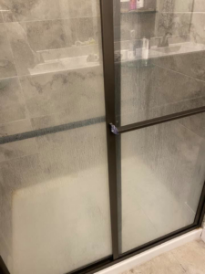 A dirty shower glass door covered in water spots and soap scum before cleaning by Tip Top Cleaning in Champaign, IL.