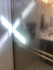 A dirty shower glass door covered in water spots and grime, ready for cleaning by Lindi's Clean Living, LLC in Tucson, AZ.