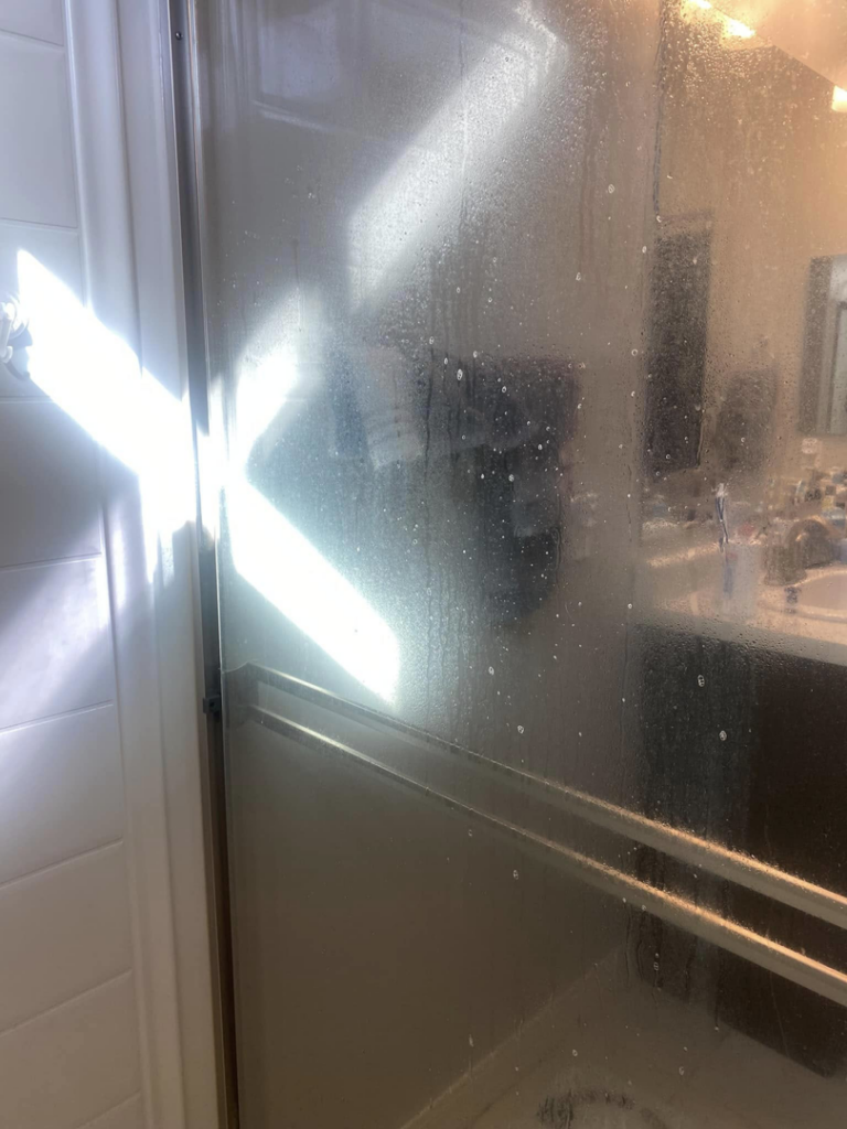 A dirty shower glass door covered in water spots and grime, ready for cleaning by Lindi's Clean Living, LLC in Tucson, AZ.