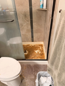 A dirty shower pan filled with brown sludge, indicating a sewage backup or severe water damage, handled by Cowboy Certified Plumbing & Water Cleanup in Lee's Summit, MO.