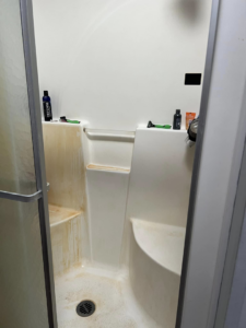 A dirty shower stall with heavy mineral stains before cleaning by Crystal's Small Town Cleaning Company, LLC in Oelwein, IA.