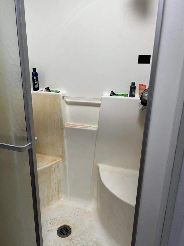 A dirty shower stall with heavy mineral stains before cleaning by Crystal's Small Town Cleaning Company, LLC in Oelwein, IA.