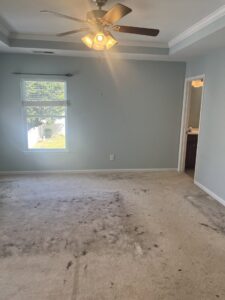 A wide shot of a bedroom with a heavily dirty and stained carpet, indicating a need for professional cleaning by Royal Madam Cleaning LLC in Charlotte, NC.