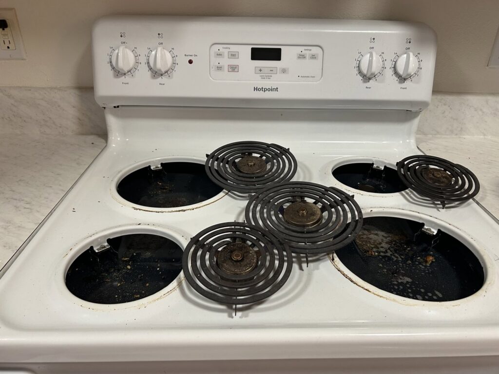 A dirty stove top with burner coils removed, showing a 'before' state for Martinez Cleaning Services in Kent, WA
