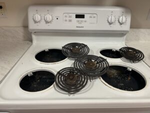 A dirty stove top with burner coils removed, showing a 'before' state for Martinez Cleaning Services in Kent, WA