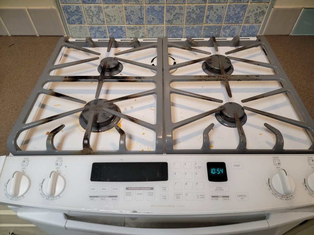 A dirty stovetop with grates, showing a 'before' state ready for a deep clean by AG Simply Clean in Concord, NC.