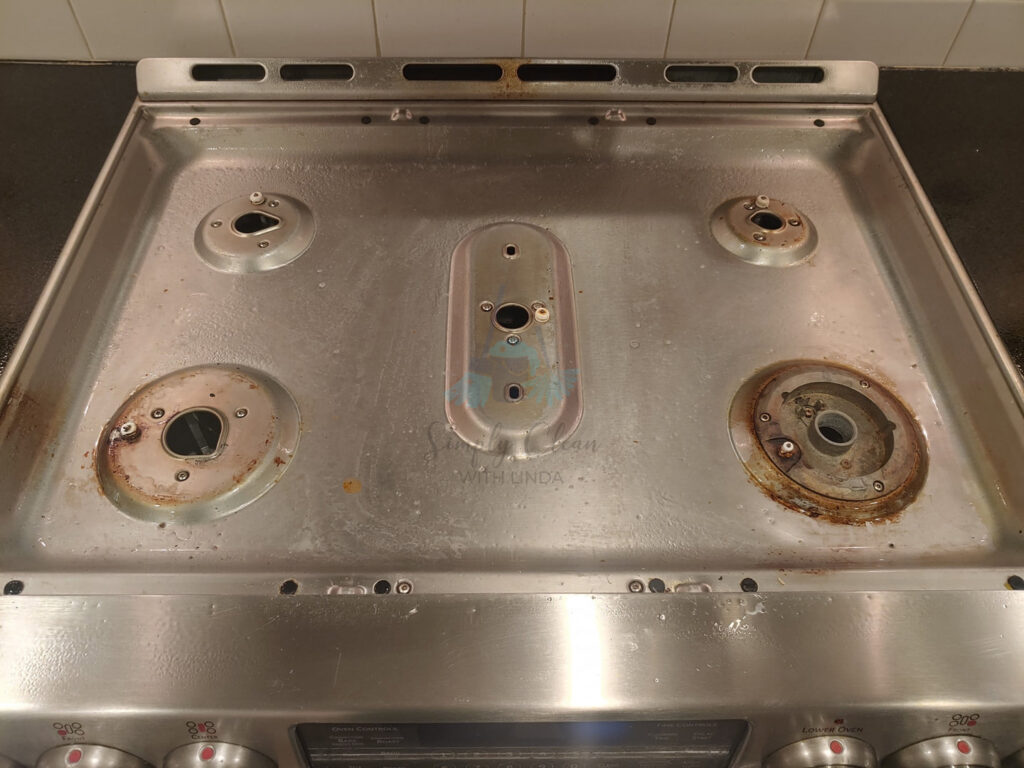 A dirty stovetop with grates removed, revealing grime underneath for a thorough cleaning by AG Simply Clean in Concord, NC.