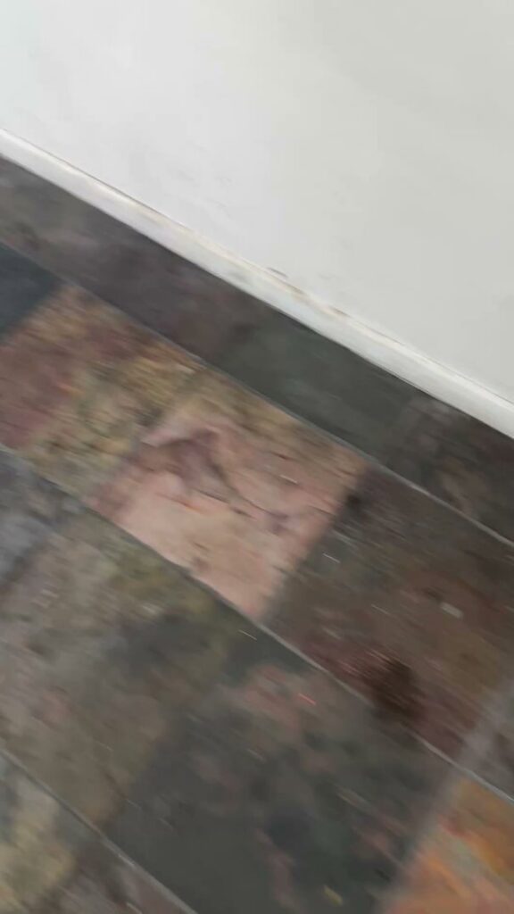 A close-up of a dirty tiled floor and baseboard, indicating a need for cleaning by Bee-Dazzled Cleaning Service in Long Beach, CA.