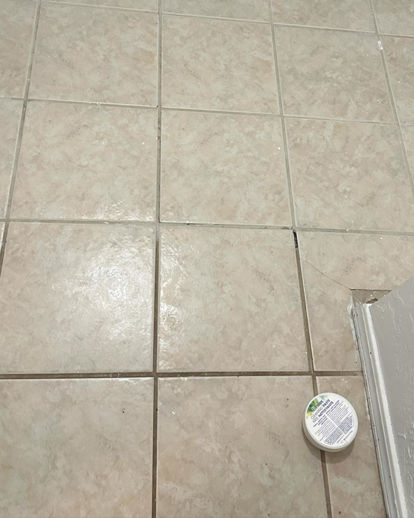 A dirty tiled floor with a cleaning product, showing the before state of a house cleaning job by Varsity Cleaning in Norman, OK.