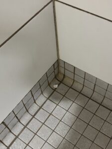 A dirty tiled floor and wall corner, showing grime before cleaning by MJ Commercial & Residential Cleaning, LLC in Cedar Rapids, IA.