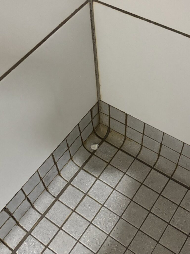 A dirty tiled floor and wall corner, showing grime before cleaning by MJ Commercial & Residential Cleaning, LLC in Cedar Rapids, IA.