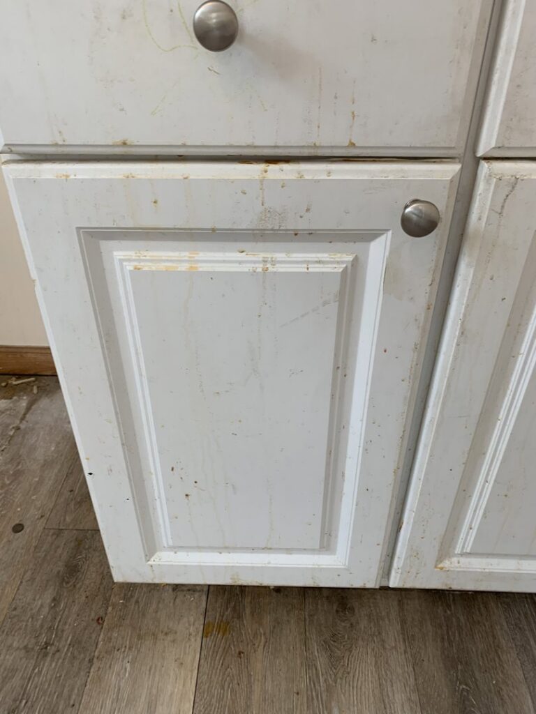 Dirty white kitchen cabinets with visible grime and stains, showing a 'before' state for Faye Cleaning Service LLC in Ankeny, IA.