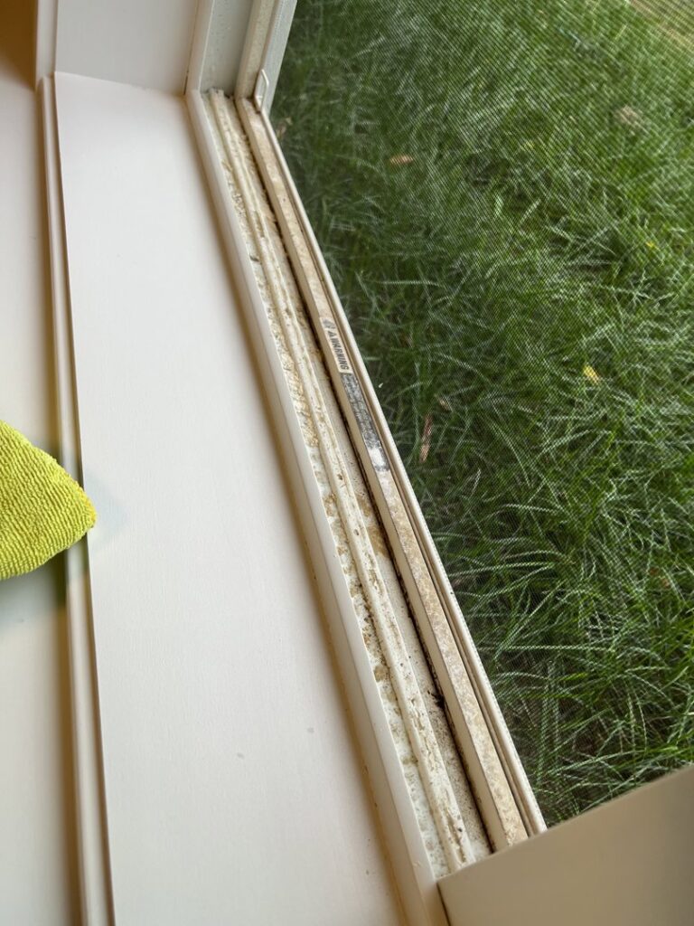 A dirty window track with accumulated debris and a cleaning cloth, showing a detailed cleaning task by Little Cubs Cleaning Services in Rochester, MN.