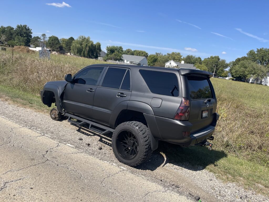 A disabled SUV missing a front wheel on the roadside, awaiting towing from Springfield Autobody and Towing in Springfield, IL.