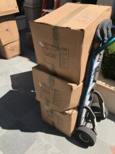 A hand truck (dolly) stacked with three cardboard moving boxes, ready for transport by The Armstrong Company in Huntsville, AL.