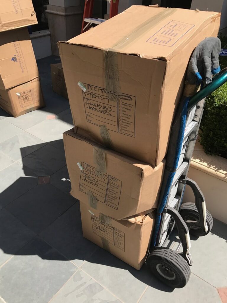 A hand truck (dolly) stacked with three cardboard moving boxes, ready for transport by The Armstrong Company in Huntsville, AL.
