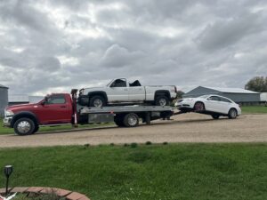 A red tow truck performing a double tow, carrying a pickup and towing a sedan, for Geely Towing in Fargo, ND.
