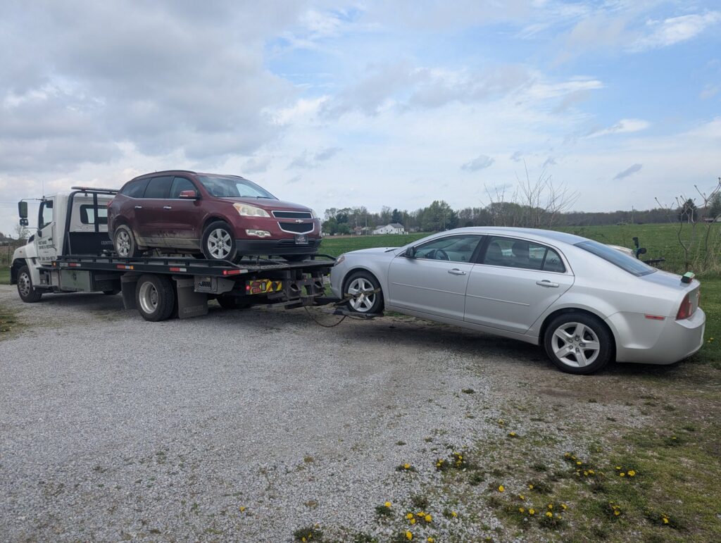 A double tow with a red SUV on the flatbed and a silver sedan on the wheel-lift by First Hand Towing & Recovery in Fort Wayne, IN.