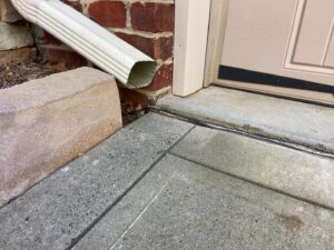 A downspout discharging water onto a concrete path, highlighting a potential drainage issue for HNO Waterproofing & Slab Lifting Pros in Concord, NC.