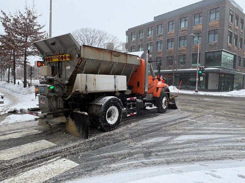 A DPW truck with a plow and salt spreader clearing and salting a road for the City of Cambridge Department of Public Works in Cambridge, MA.