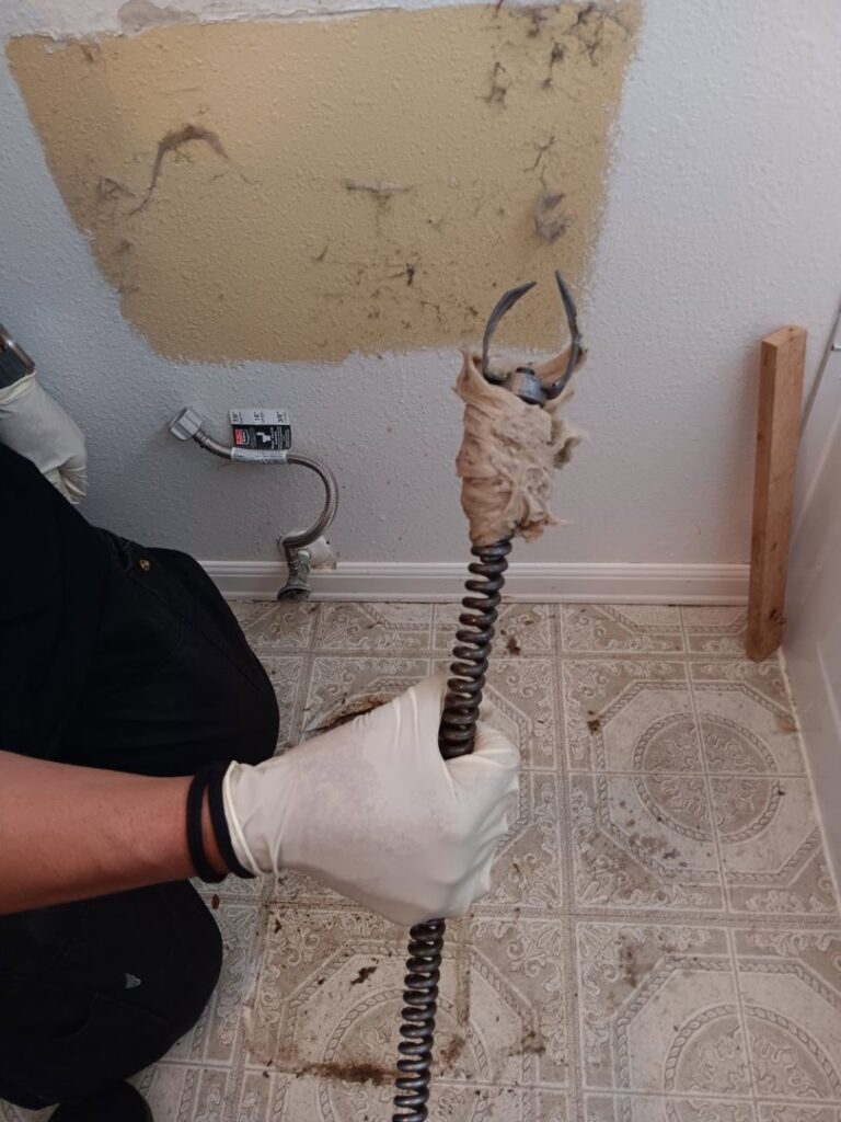 A drain cleaning tool with debris from a clogged pipe, showing water damage on a bathroom floor and ceiling in Tulalip, WA.